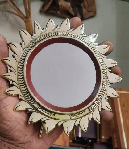 A finished metal mirror held up and checked by hand